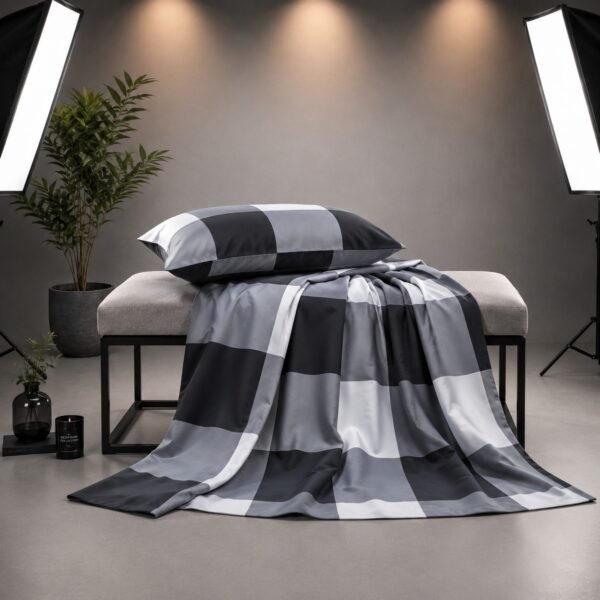 Neatly folded grey and black buffalo check bedspread set with pillowcases stacked on a studio table